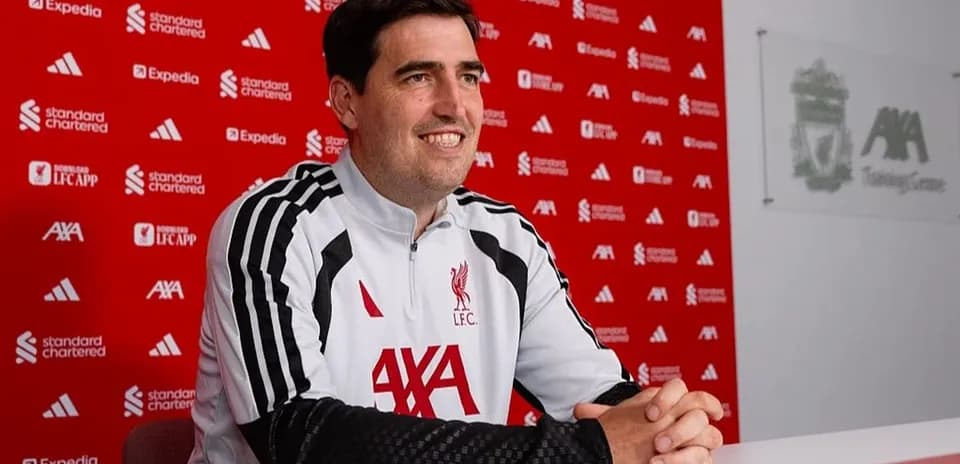 Manager seated at press conference table with Liverpool backdrop