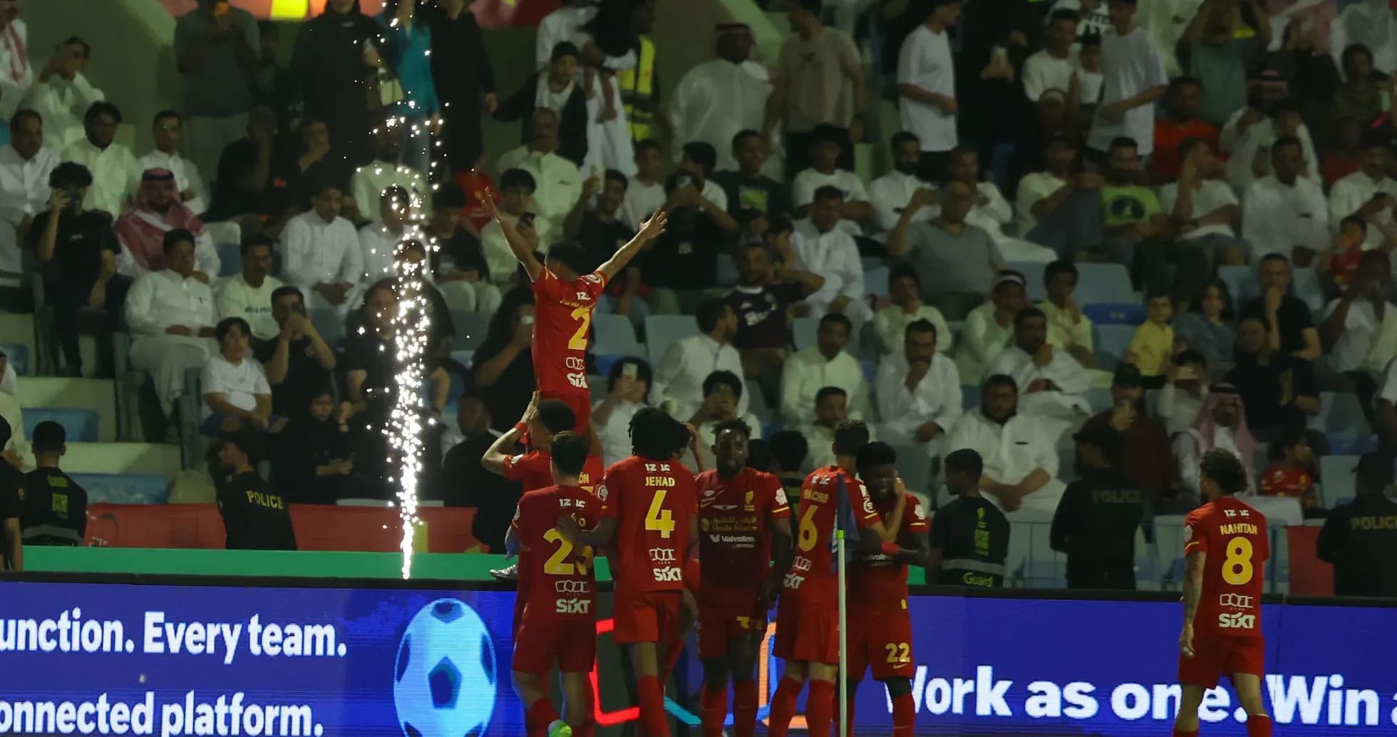 Players celebrating a goal with fireworks in stadium