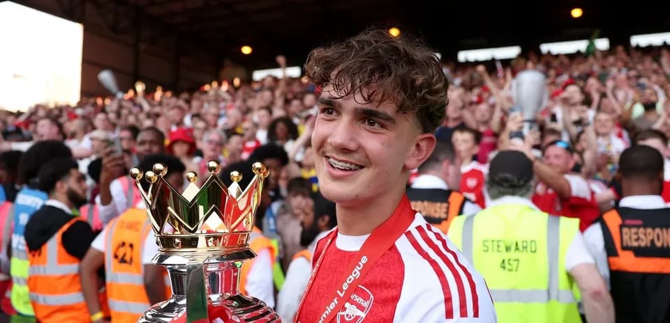 Player holding Premier League trophy with celebrating fans