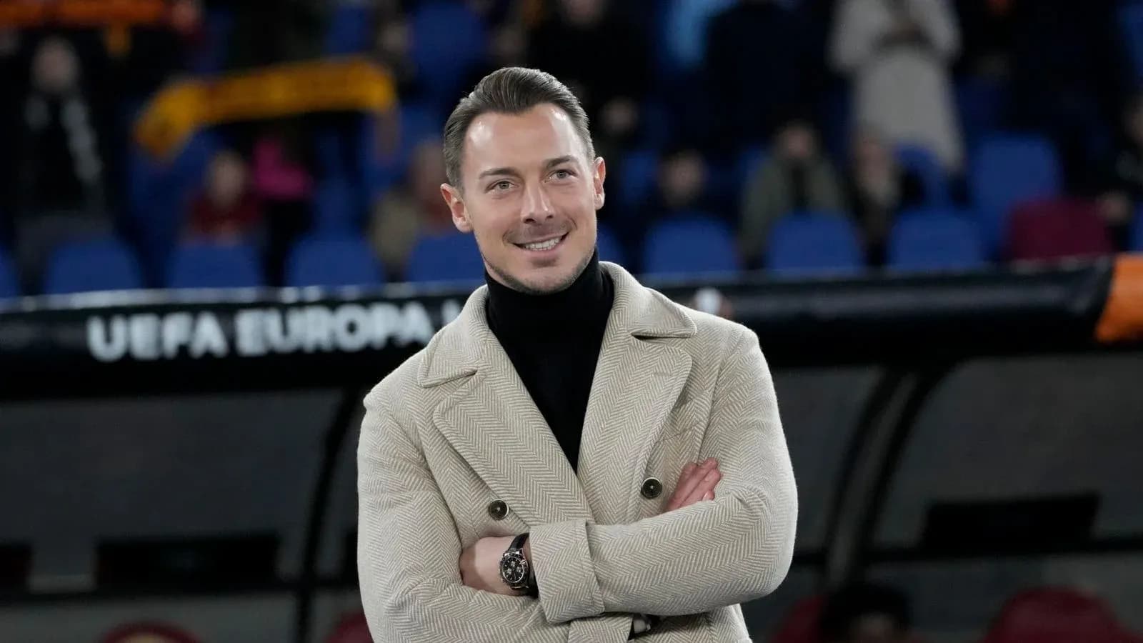 Man in stylish coat smiling at the stadium