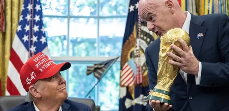 Man holding World Cup trophy with another man watching