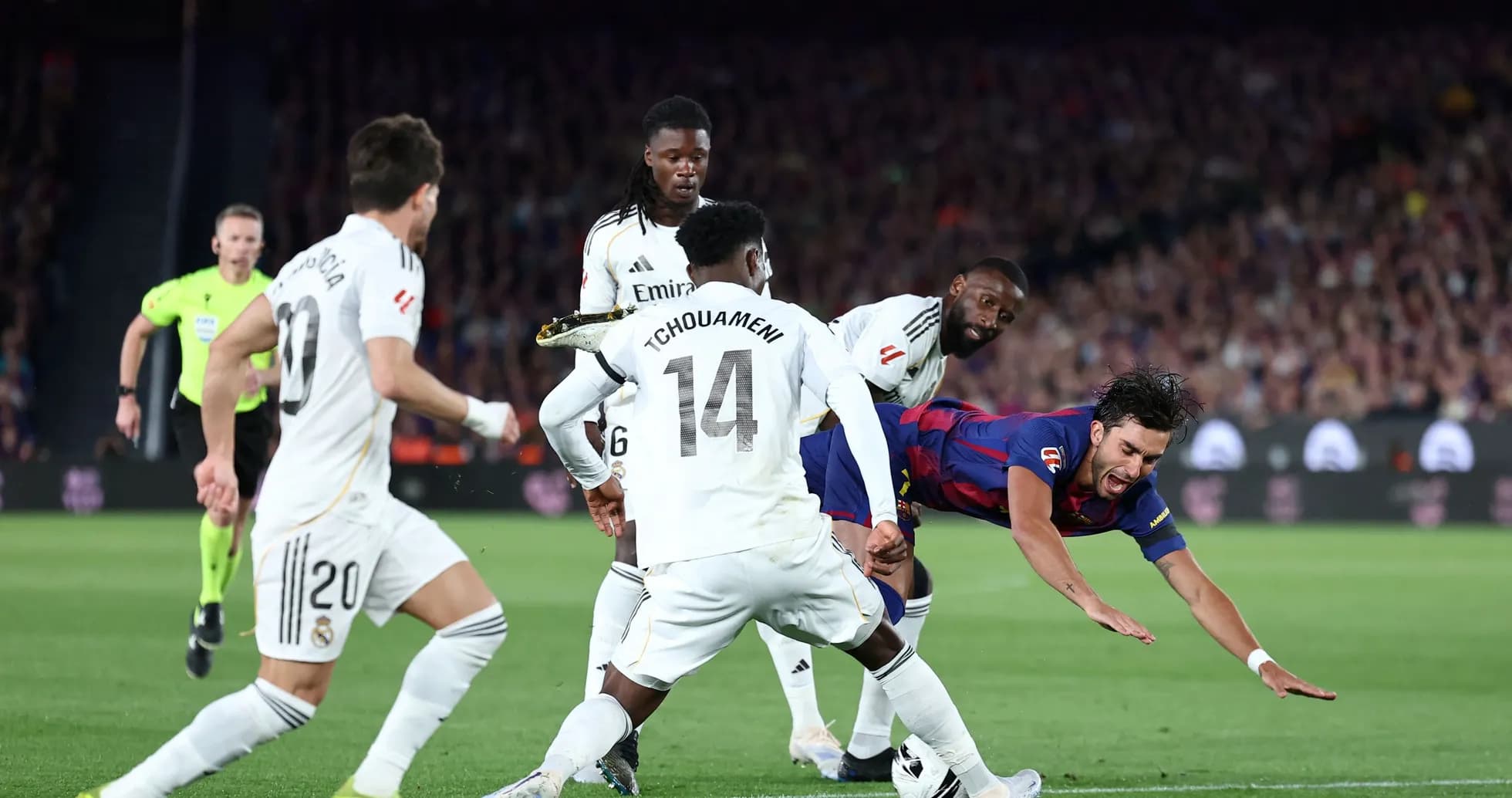 Barcelona player falling while challenged by Real Madrid defenders