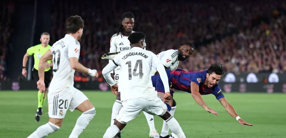 Barcelona player falling while challenged by Real Madrid defenders