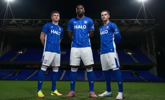 Three players posing in blue home kits on pitch
