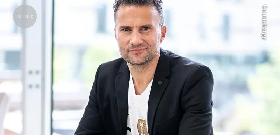 Man in blazer seated indoors with a FIFA badge
