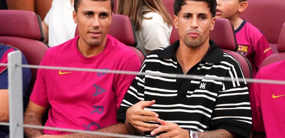 Two men seated in stadium wearing team jerseys