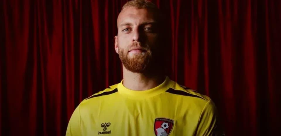 Goalkeeper wearing yellow kit in front of red backdrop