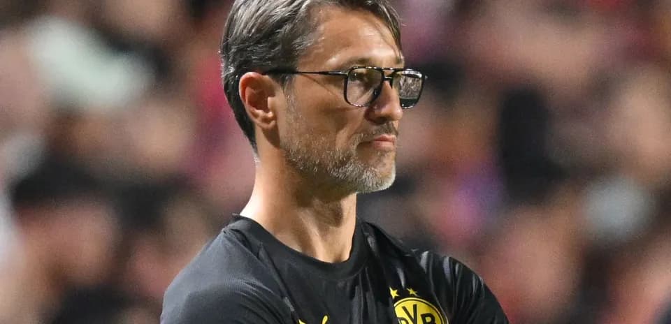 Coach observing match from sidelines in black attire