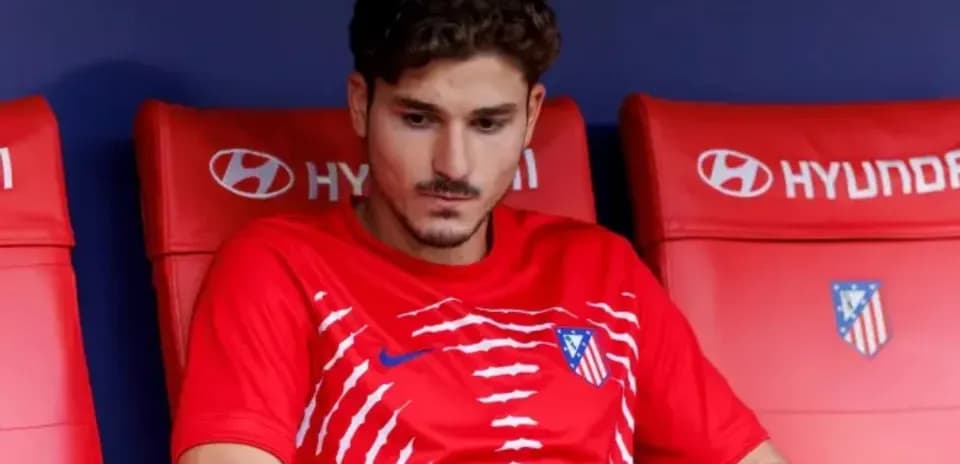 Player sitting on bench wearing Atletico Madrid jersey