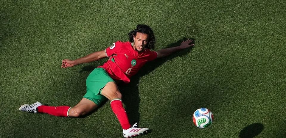 Player in red and green uniform reaching for soccer ball