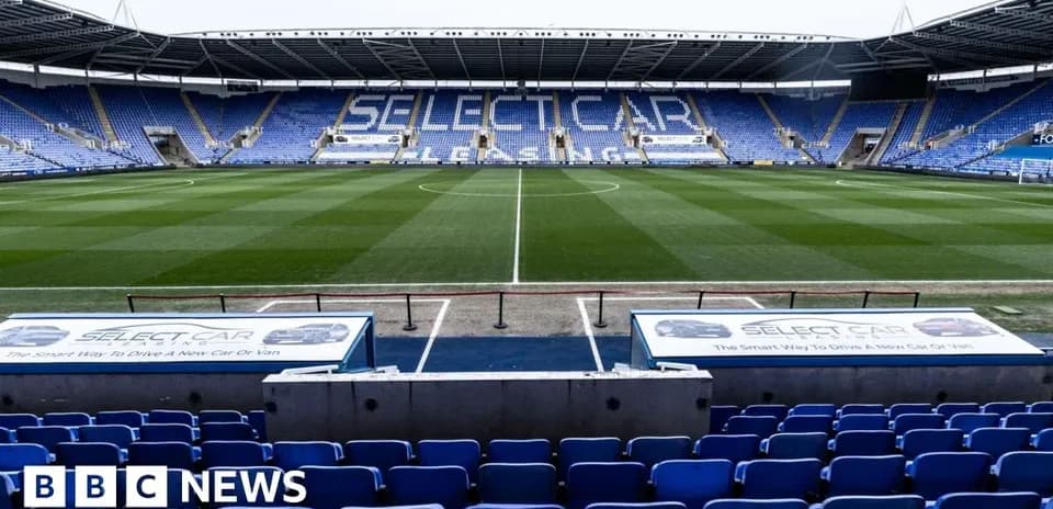 Empty football stadium with blue seating and grass pitch