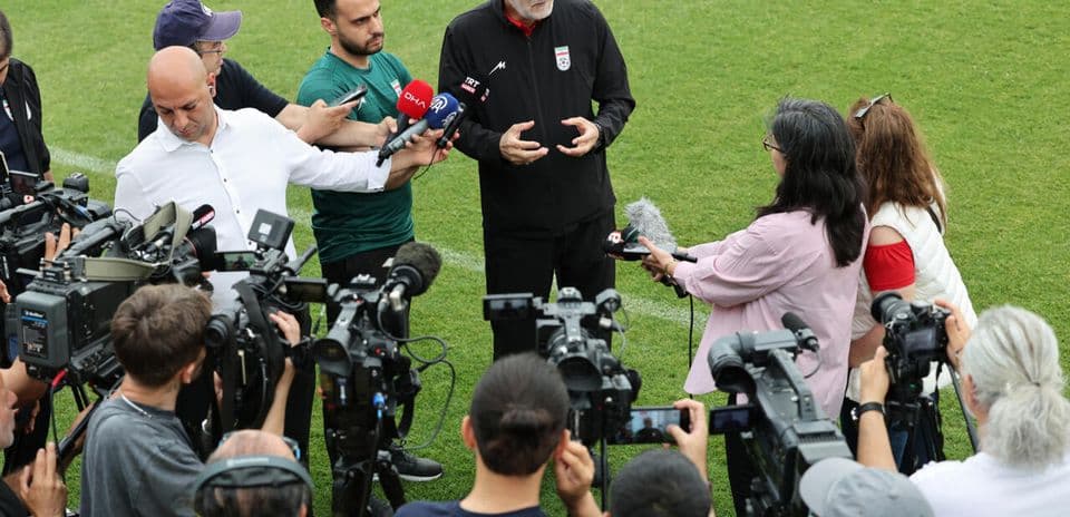 Coach giving interview surrounded by journalists and cameras