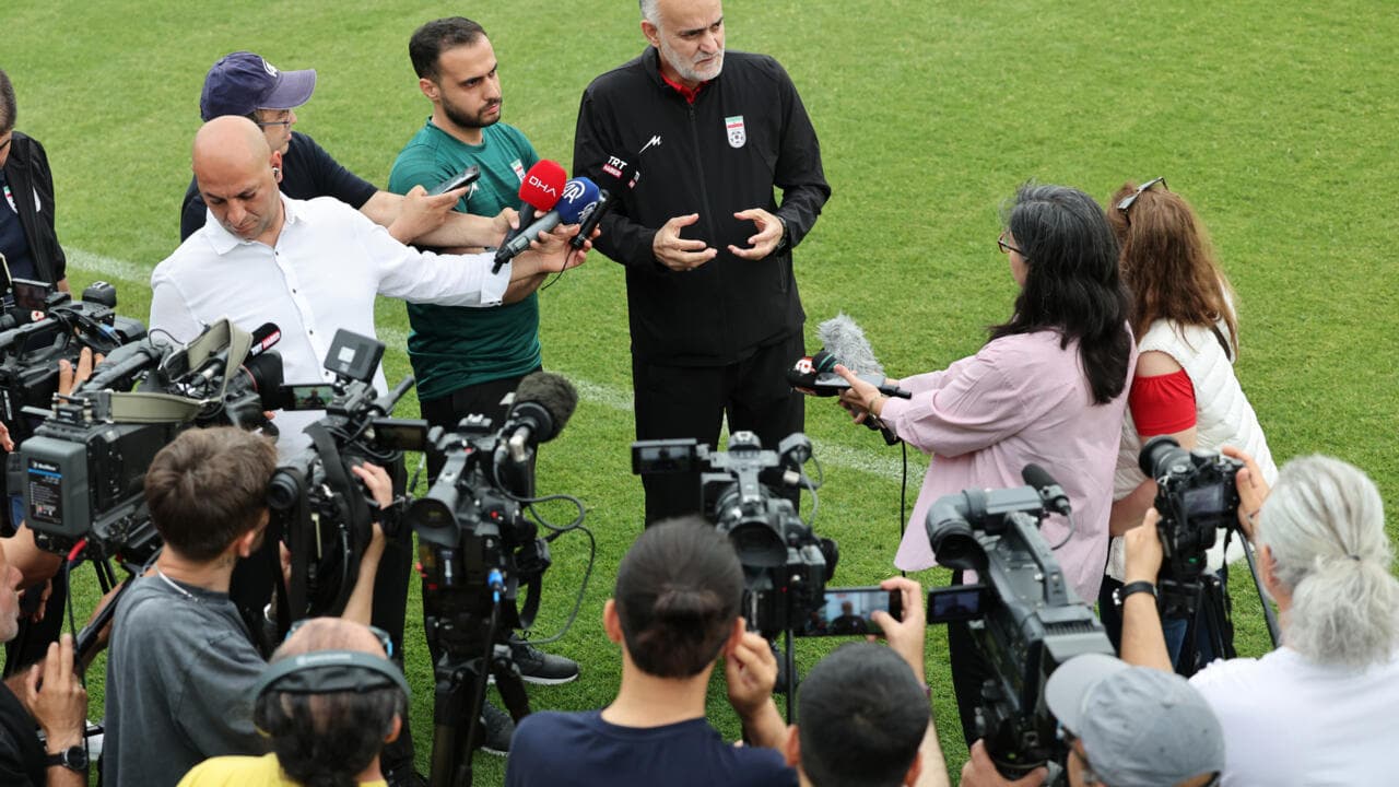 Coach giving interview surrounded by journalists and cameras