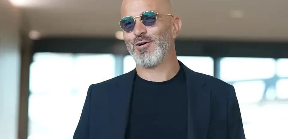 Man wearing sunglasses and a dark suit smiling