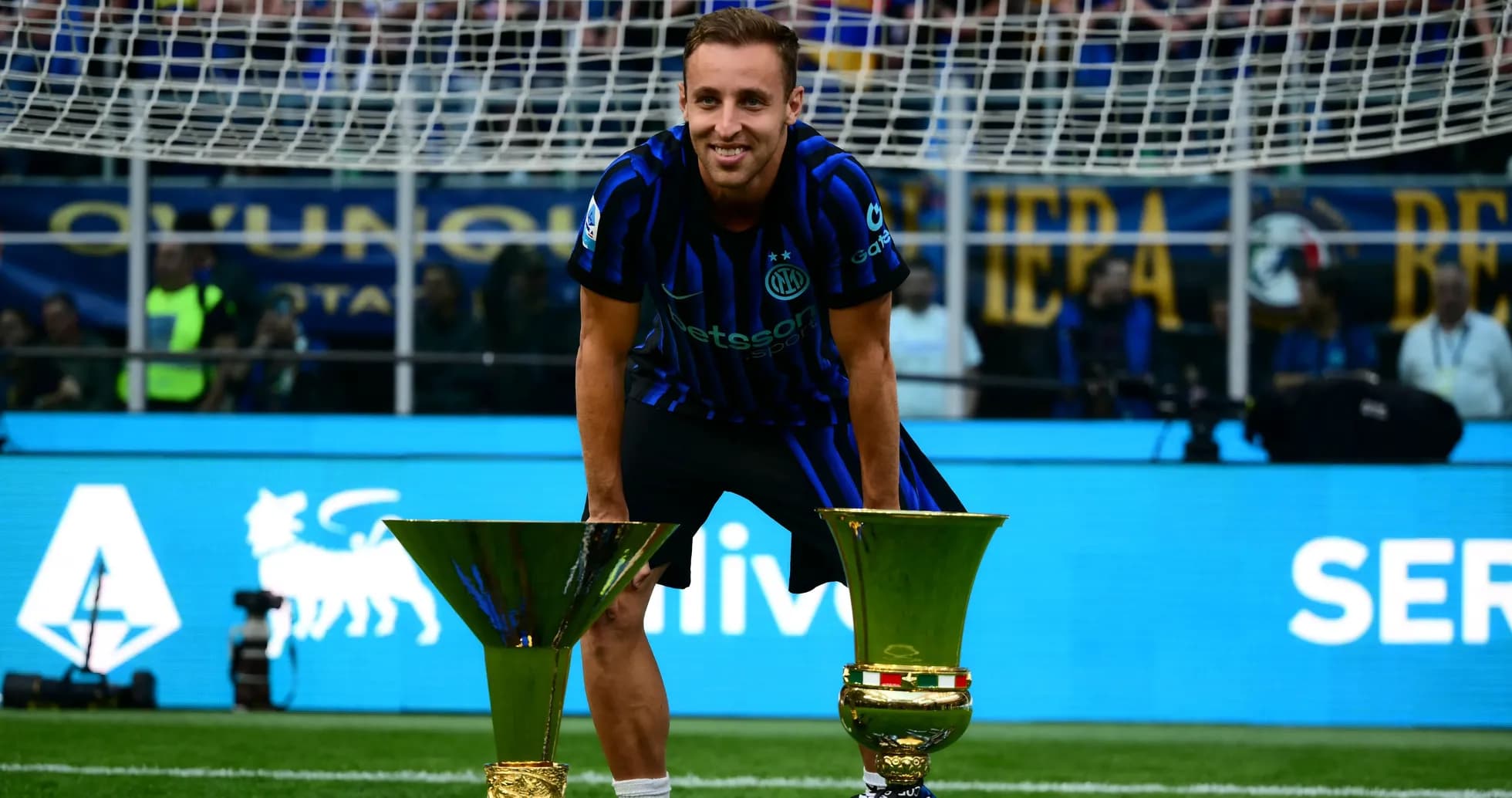 Player celebrating with two trophies on the pitch