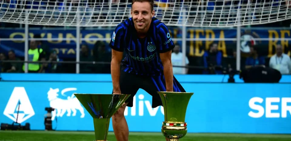 Player celebrating with two trophies on the pitch