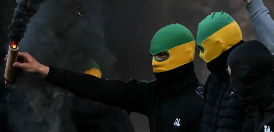 Masked individuals holding flare in smoky environment