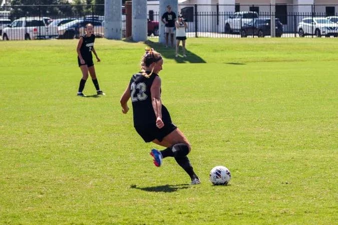 Player in black jersey kicking soccer ball on field