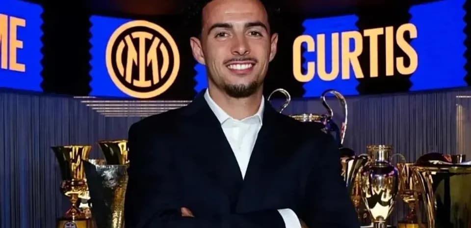 Person posing in front of trophies and club logo