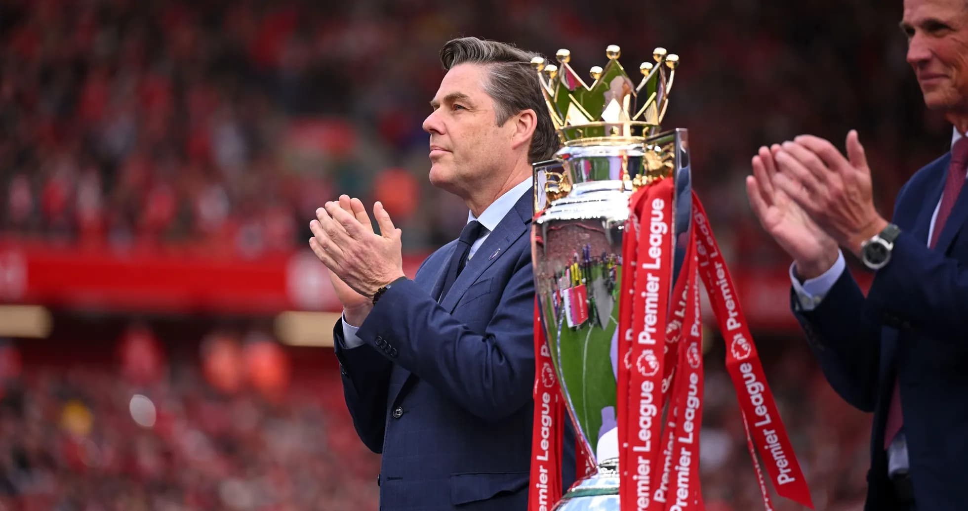 Person applauding next to Premier League trophy