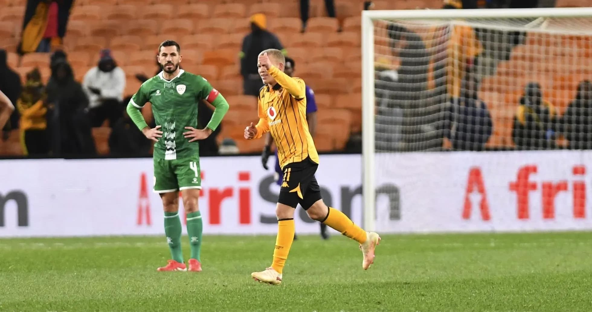 Player celebrating while another looks on, stadium background