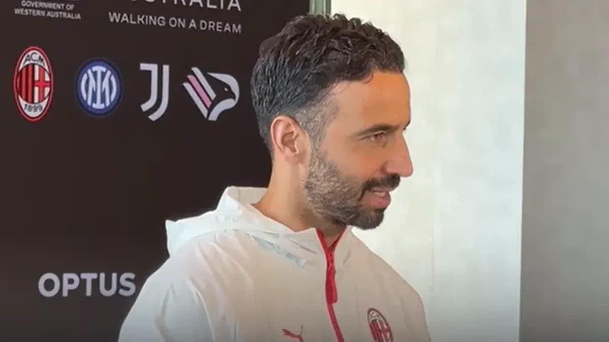 Man speaking during press conference with team logos