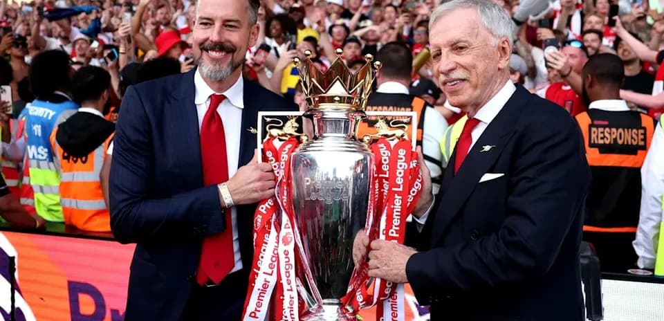 Two officials holding Premier League trophy with fans celebrating