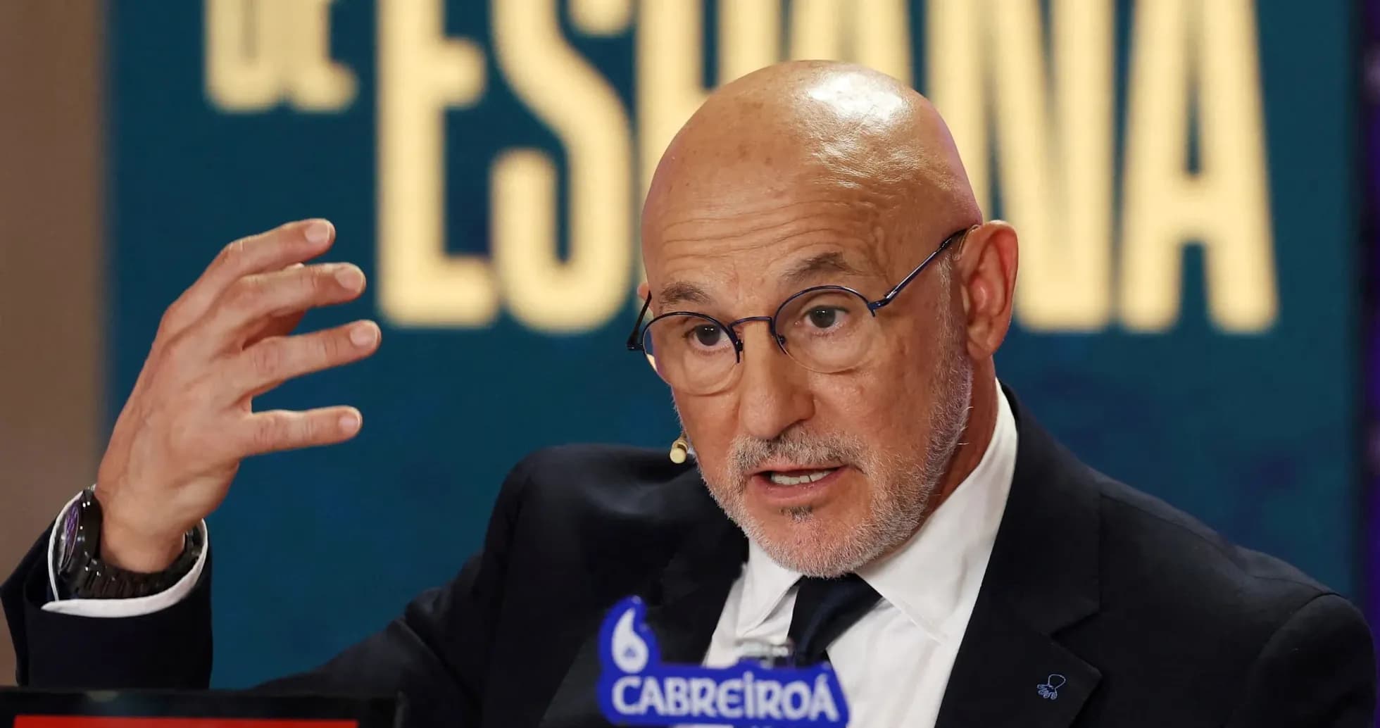 Man speaking at press conference with gesturing hand