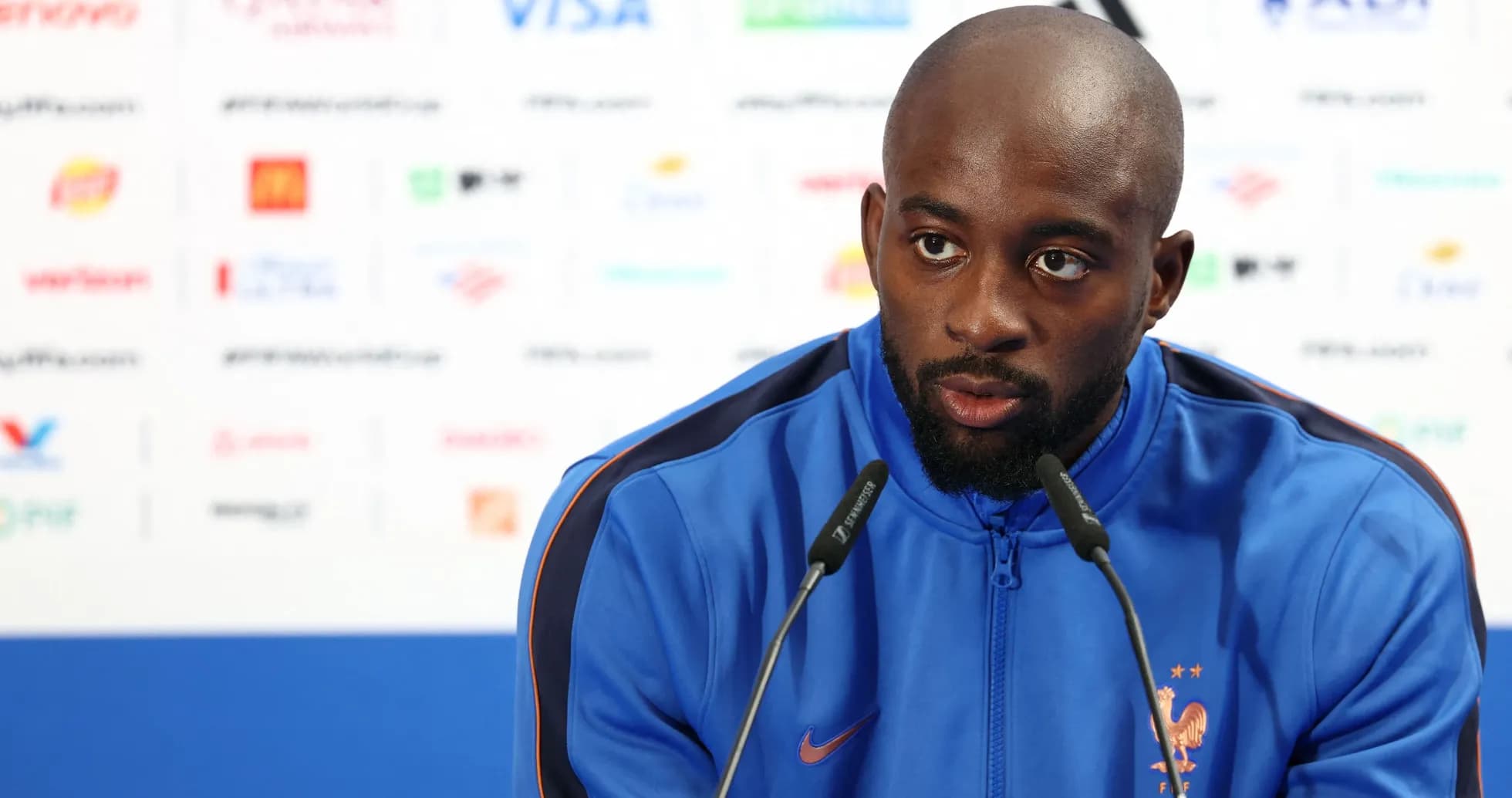 Player speaking at press conference in blue jacket