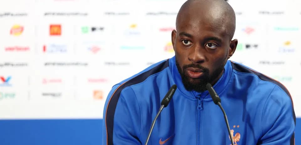 Player speaking at press conference in blue jacket