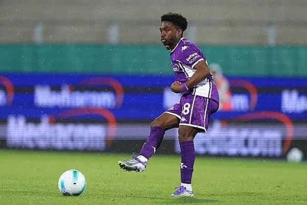 Player in purple kit dribbling soccer ball on field