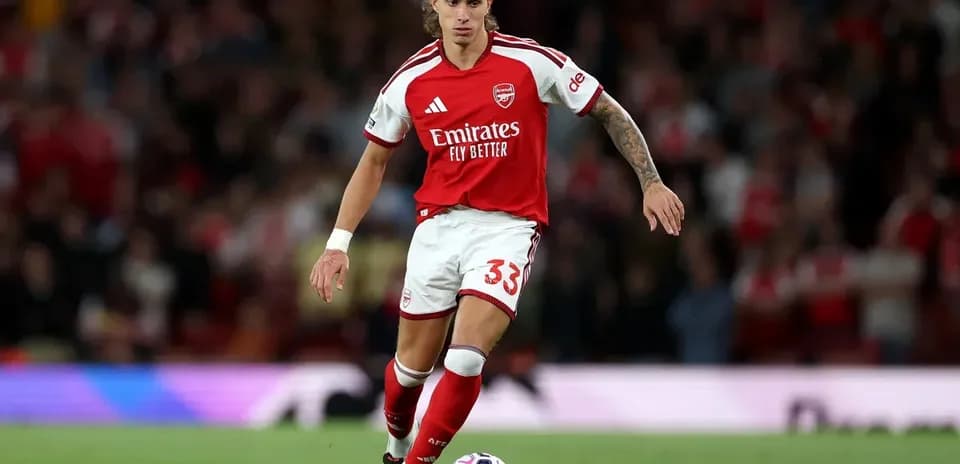Player in Arsenal kit dribbling ball on pitch