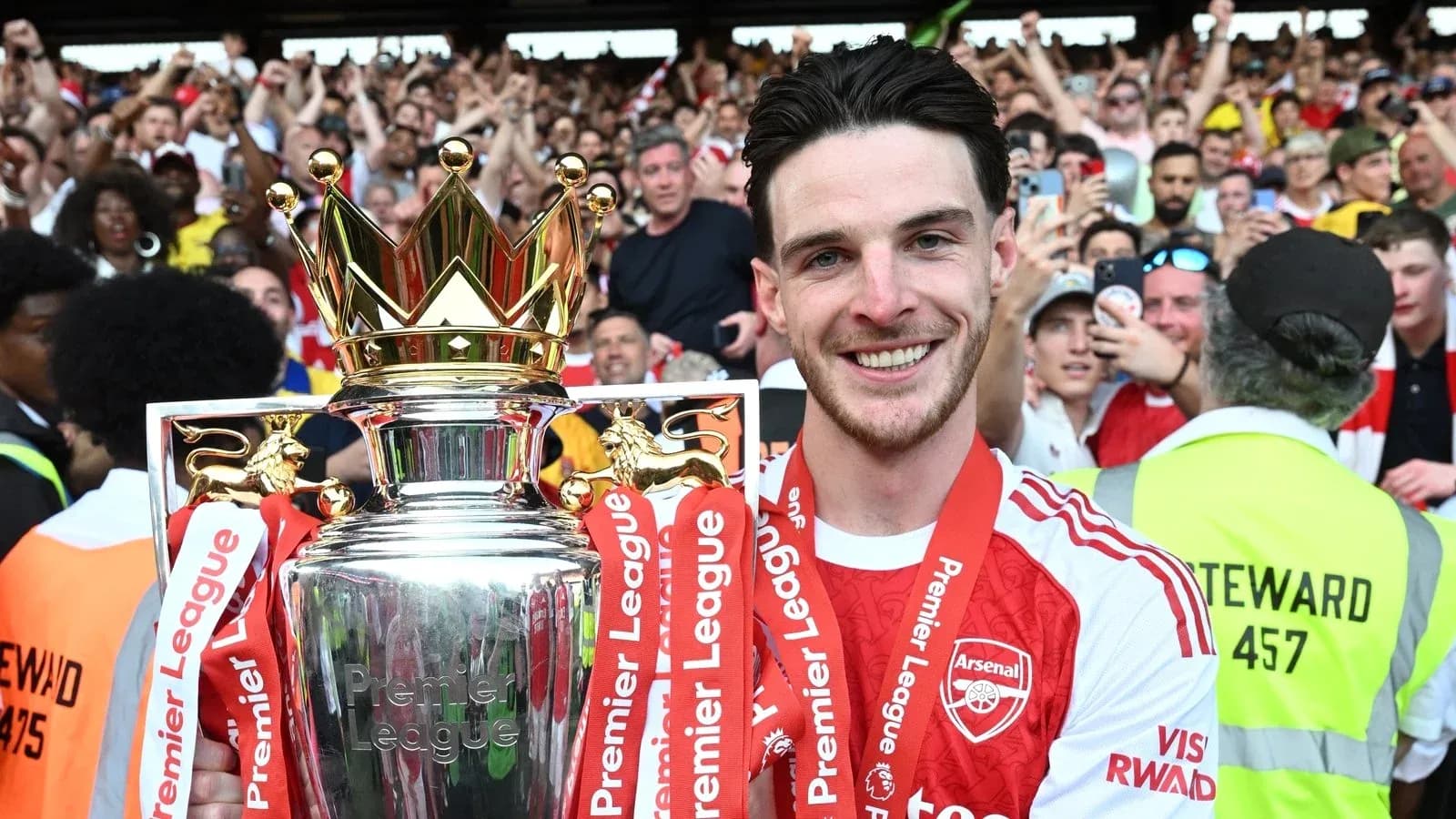 Player holding Premier League trophy with fans cheering
