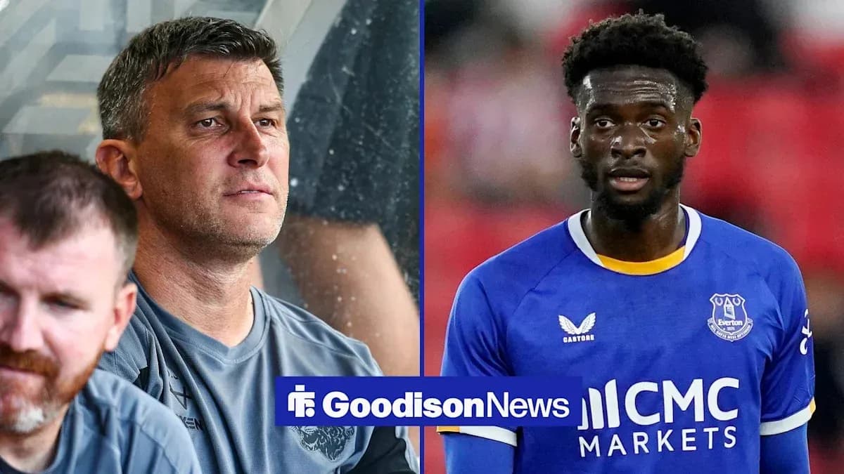 Coach observing match alongside Everton player in uniform