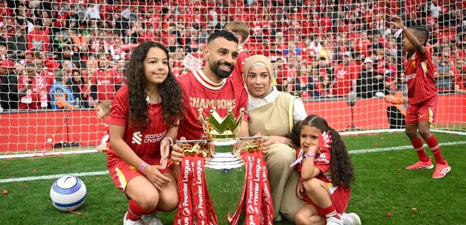 Player holding Premier League trophy with family on pitch