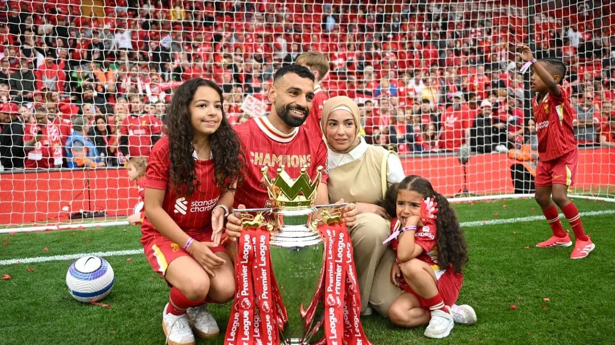 Player holding Premier League trophy with family on pitch