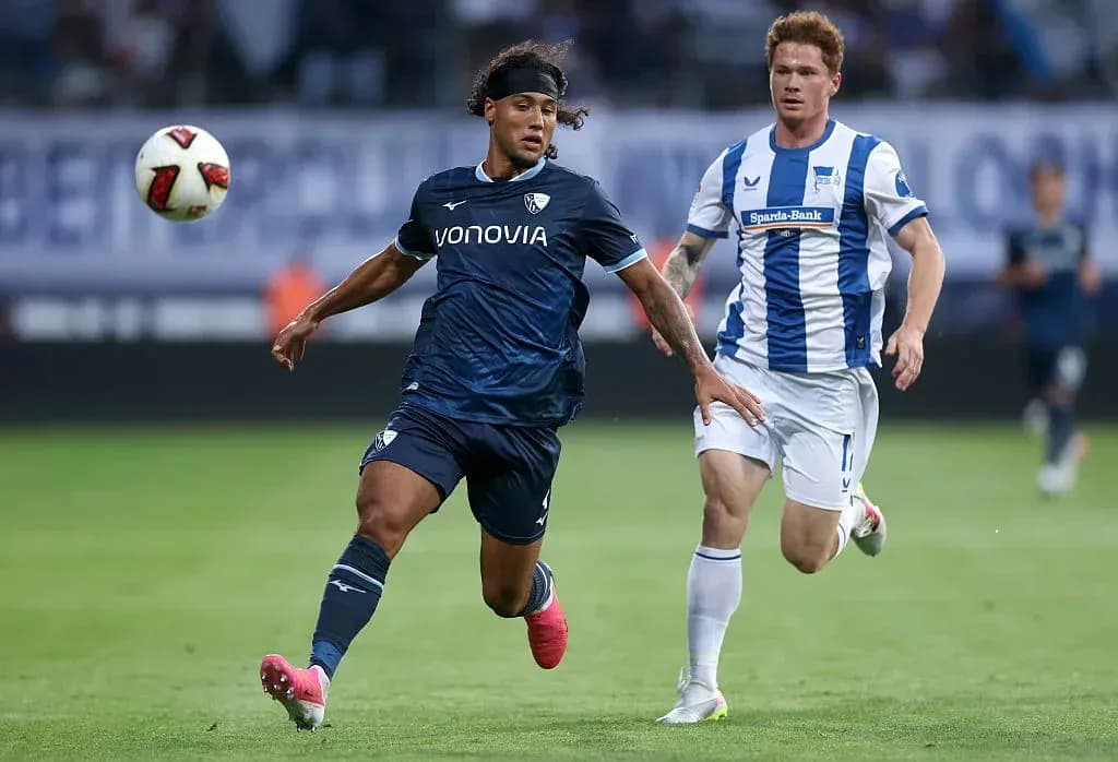 Player in dark kit chasing ball with opponent nearby