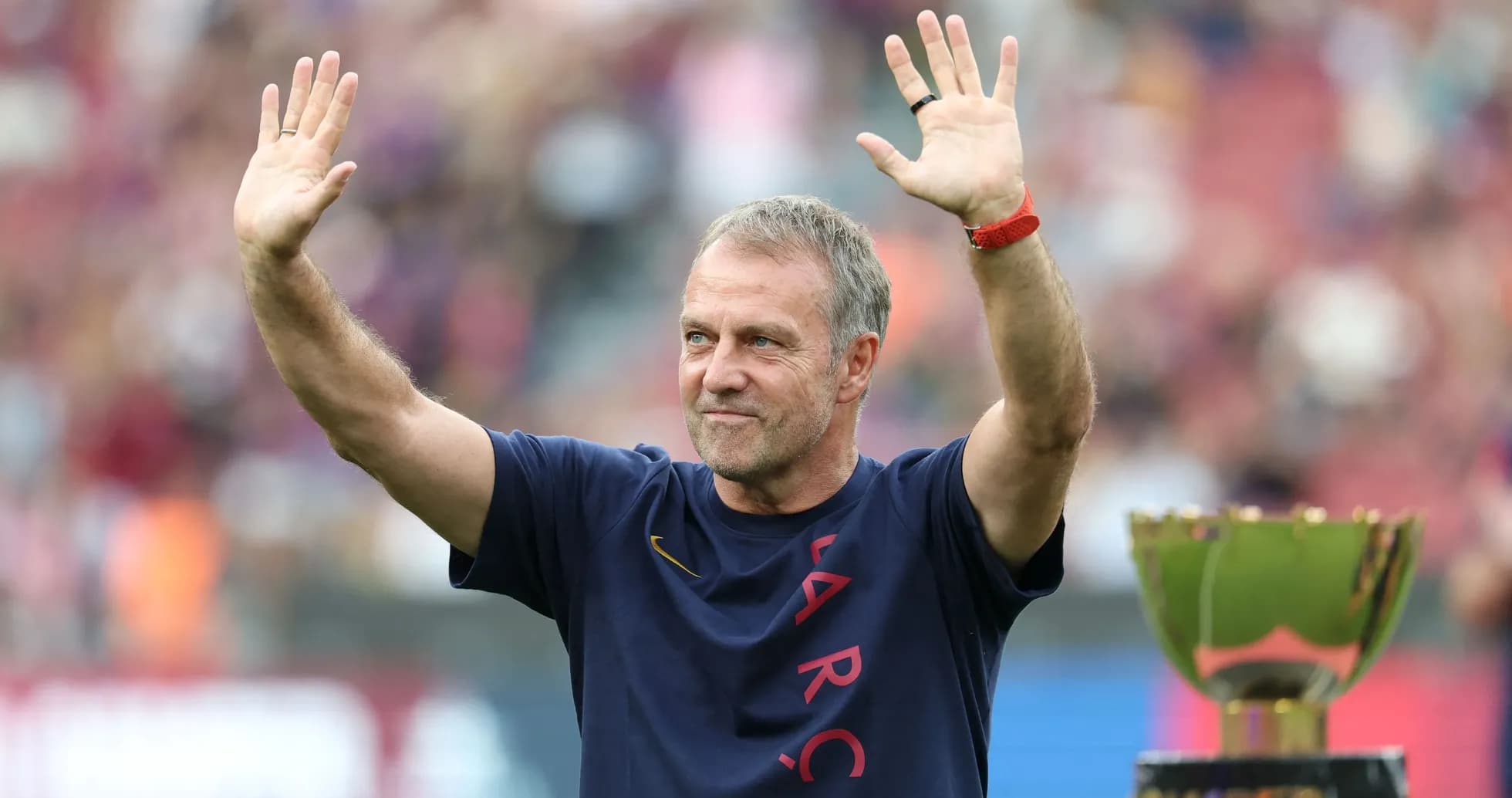 Coach waving to fans beside a trophy