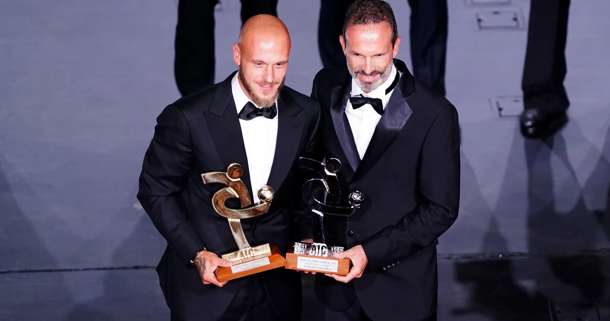 Two men in tuxedos holding awards at ceremony