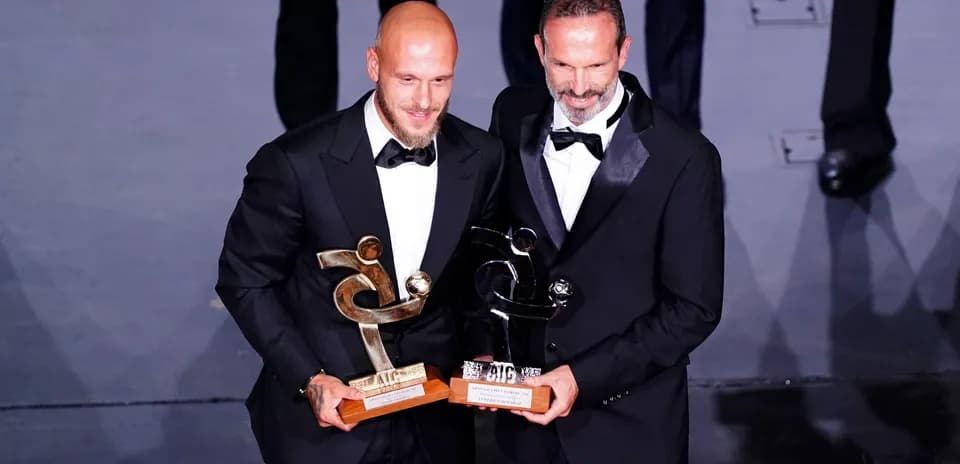 Two men in tuxedos holding awards at ceremony