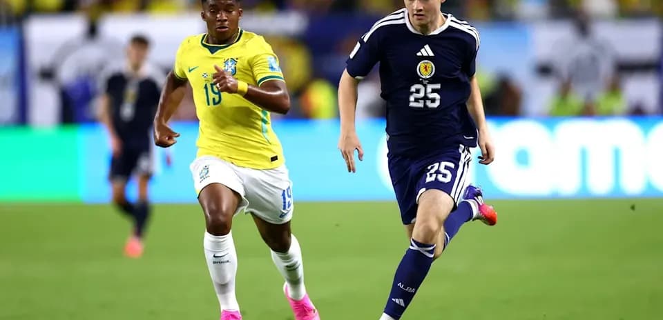 Player from Scotland dribbling ball, Brazilian player chasing