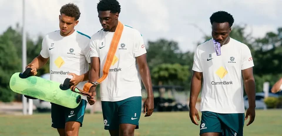 Three Australian players carrying training equipment