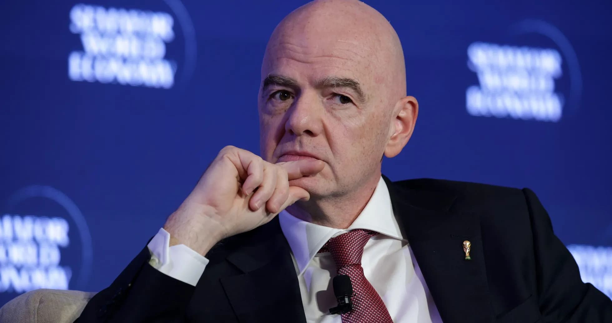 Man speaking at a conference with FIFA logo pin
