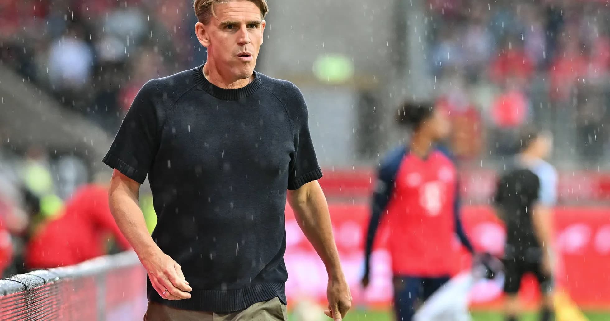 Coach walking along sideline in rainy match