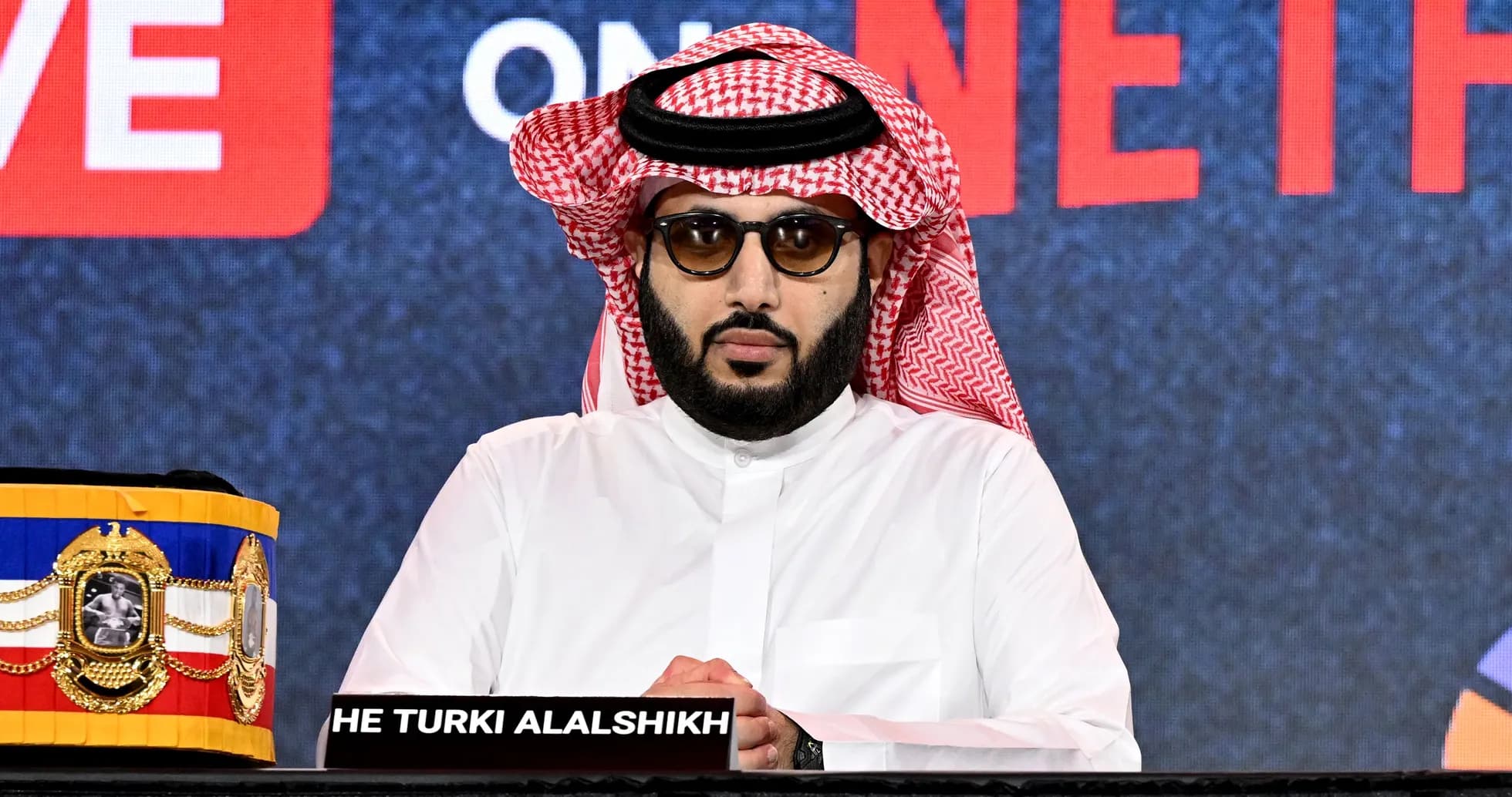 Man in traditional attire at press conference table Man in traditional attire at press conference table