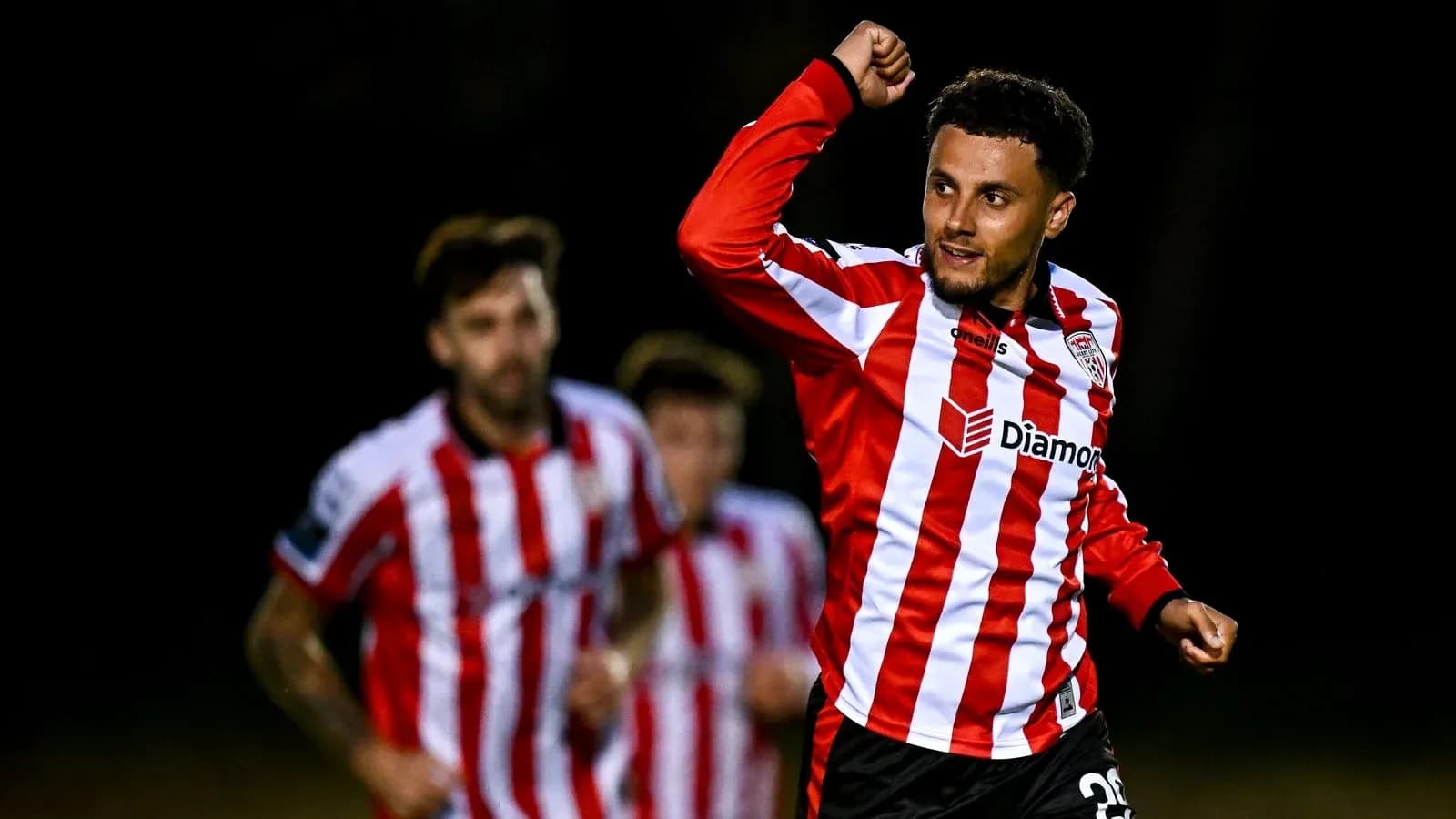 Player celebrating goal with teammates in background Player celebrating goal with teammates in background