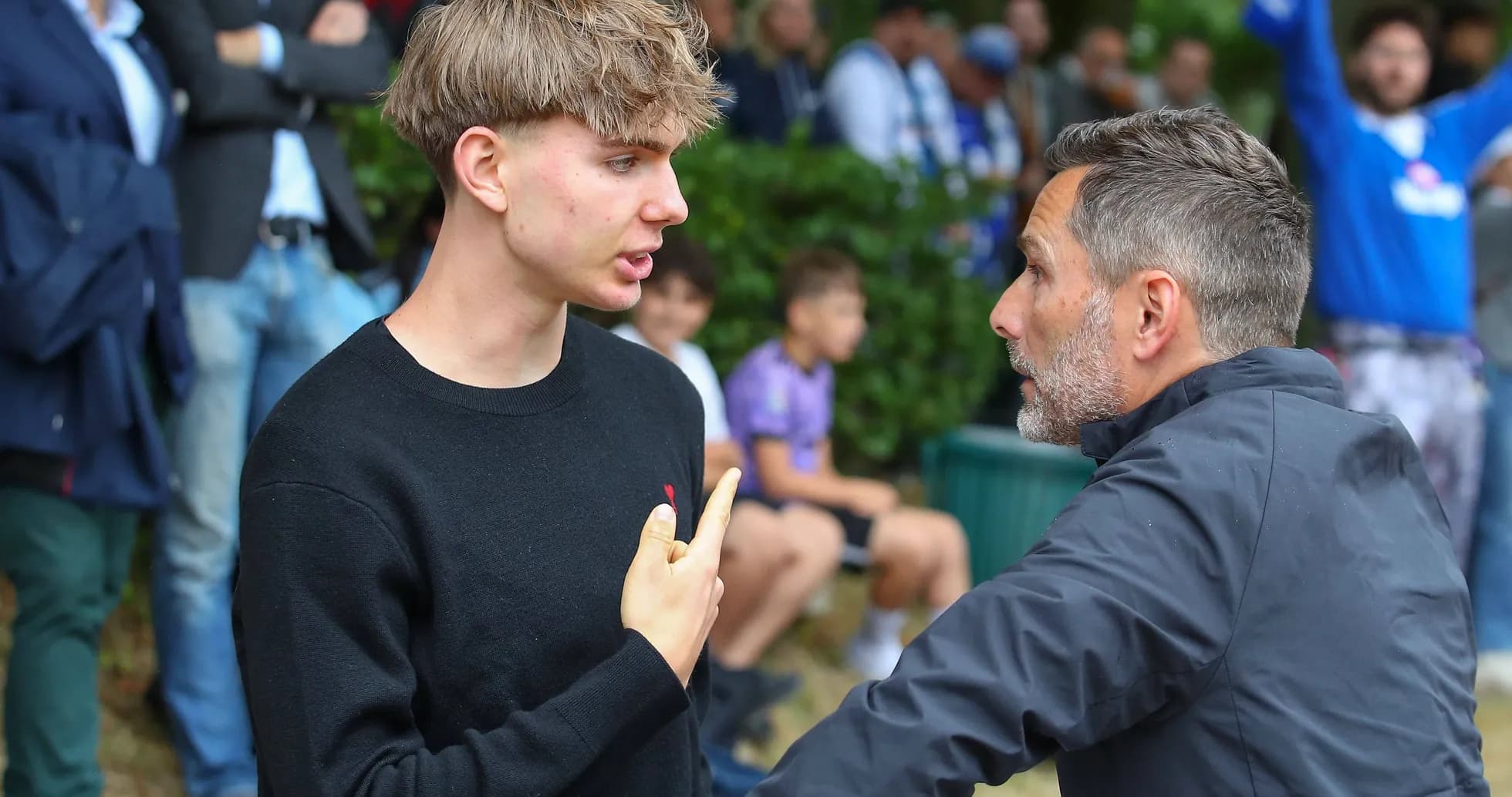 Two individuals discussing near a crowd of spectators Two individuals discussing near a crowd of spectators